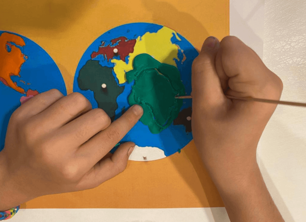Las manos de un niño dando forma a los continentes siguiendo el código de color Montessori.